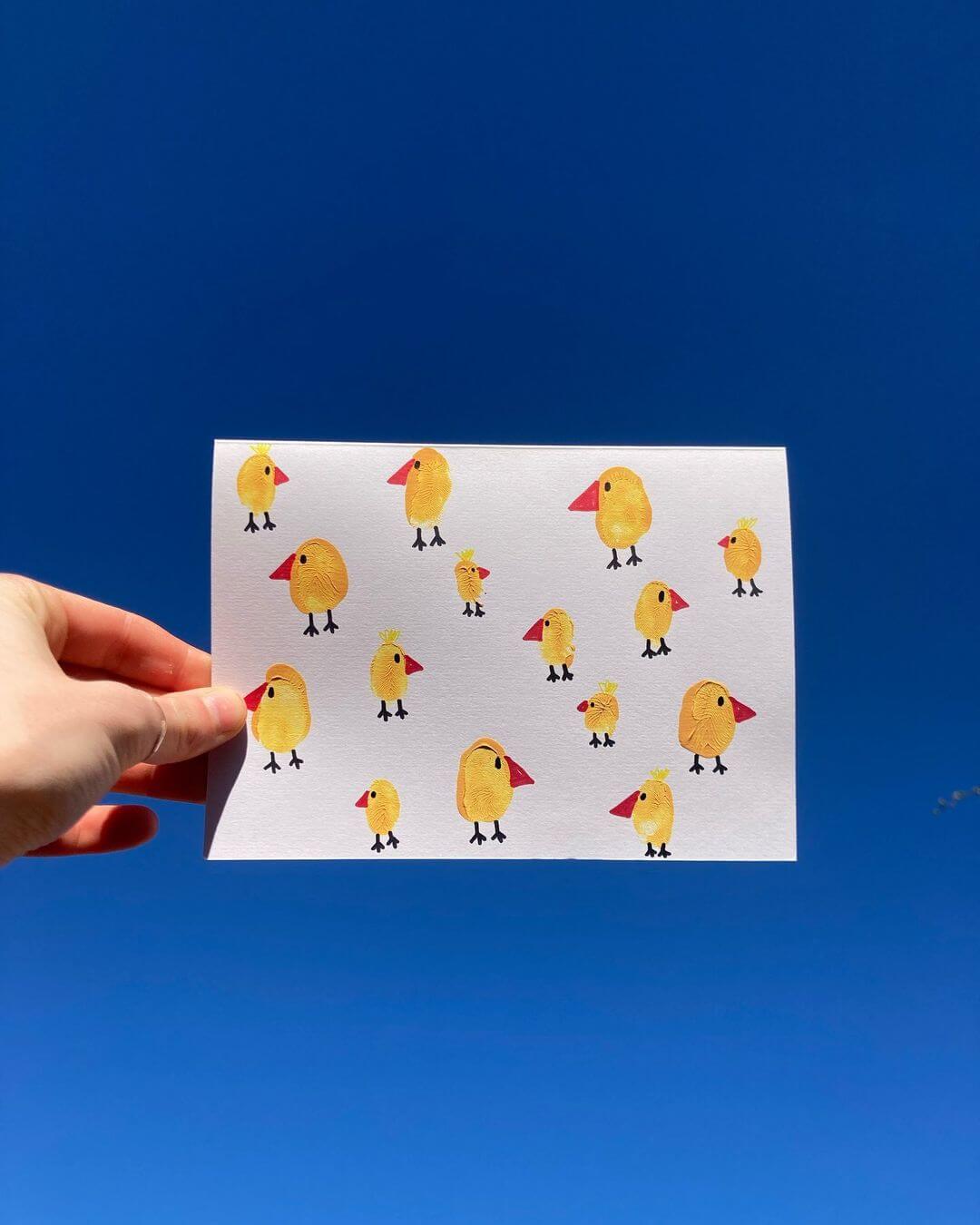 Hand holding finger painted Easter chickens on paper in the sky.