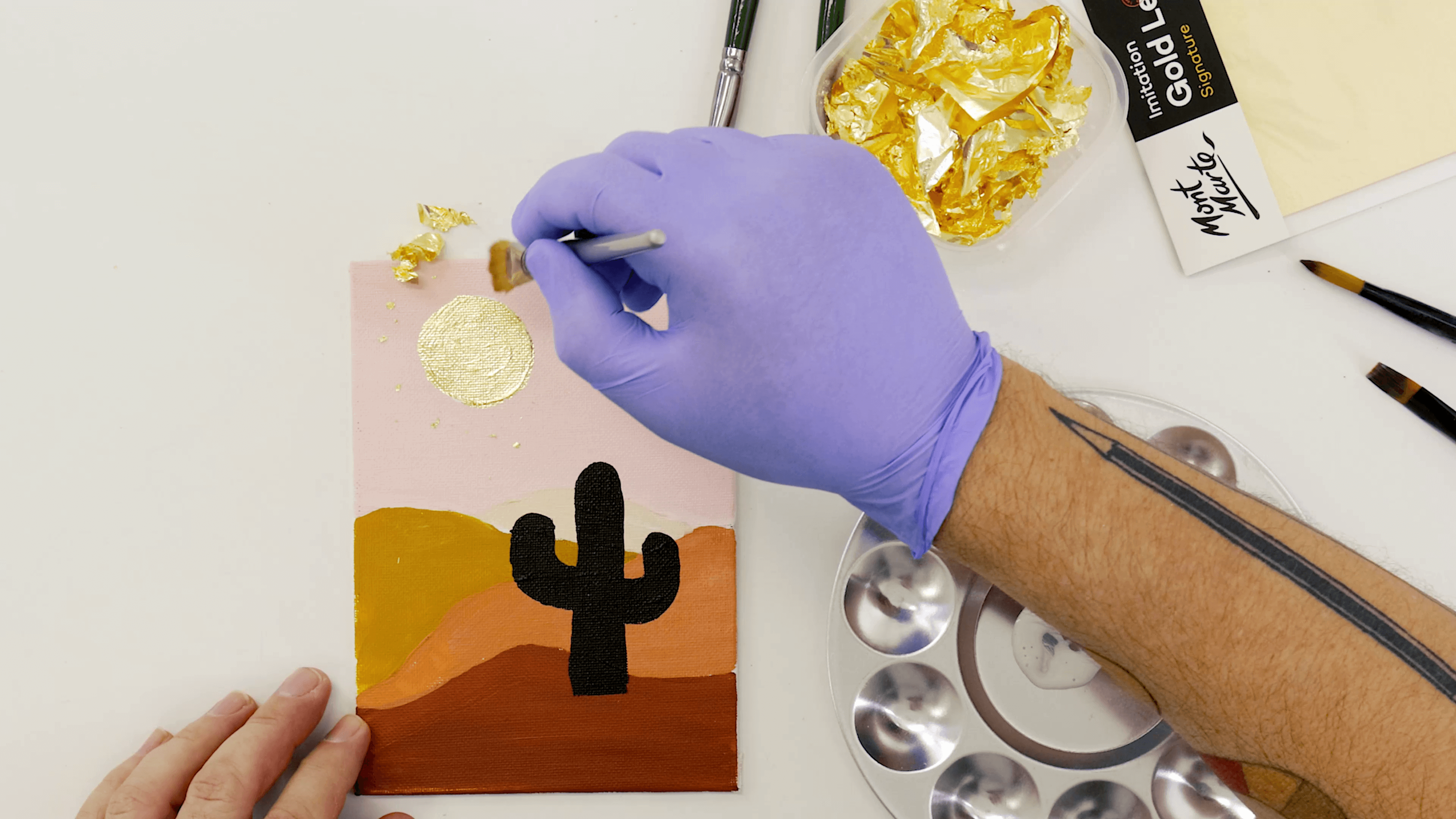 Hand placing gold leaf in a small surface area on a gouache artwork.