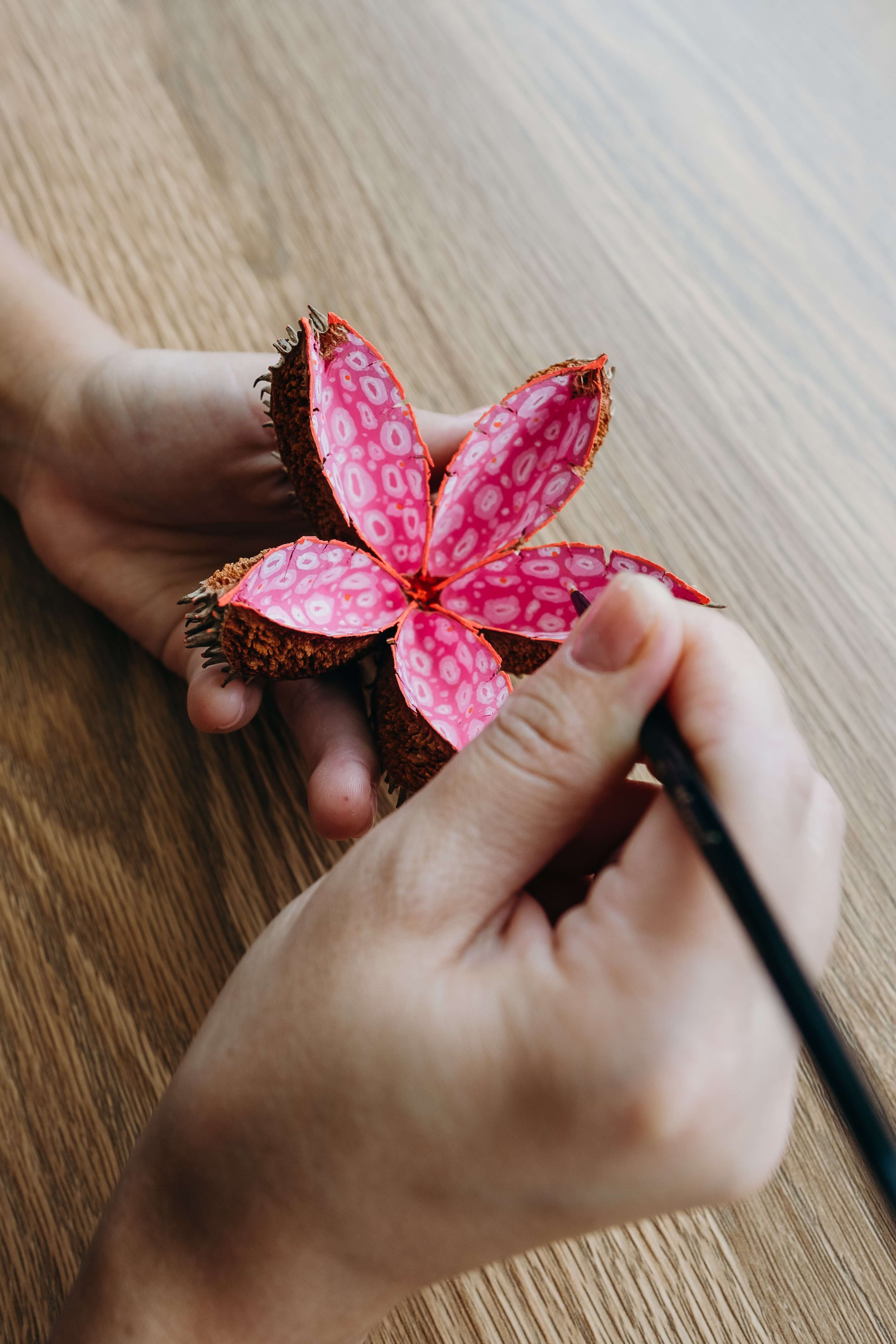 7. Hands intricately painting a leaf to look like a pink flower.