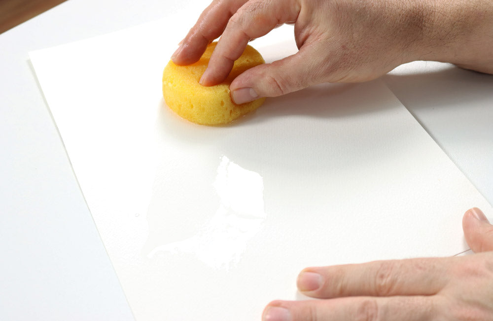 Hand using wet sponge on paper. 