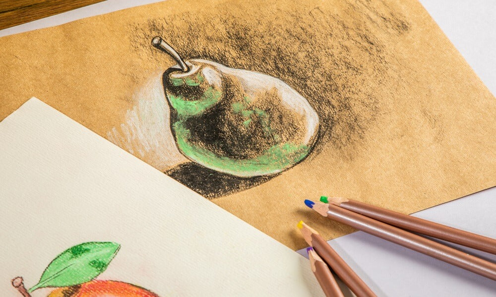 Four pastel pencils of various colours laying on top of an artwork of a pear.