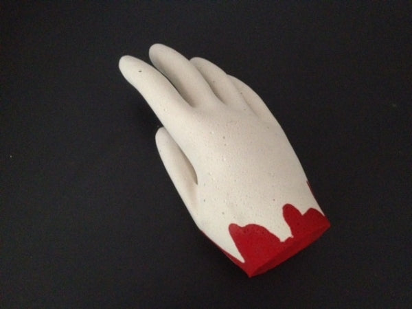 A hand made from plaster with red paint on it to look like blood, laying on a black table.