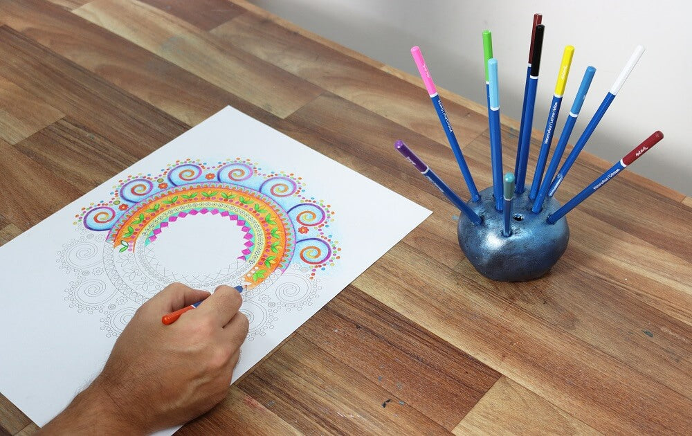 Blue metallic pencil holder with coloured pencils and hand colouring in.