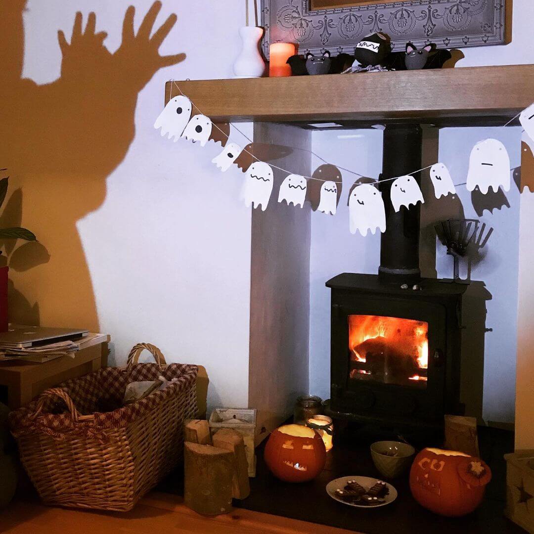 A fireplace with a ghost Halloween garland and a silhouette of a monster on the wall.