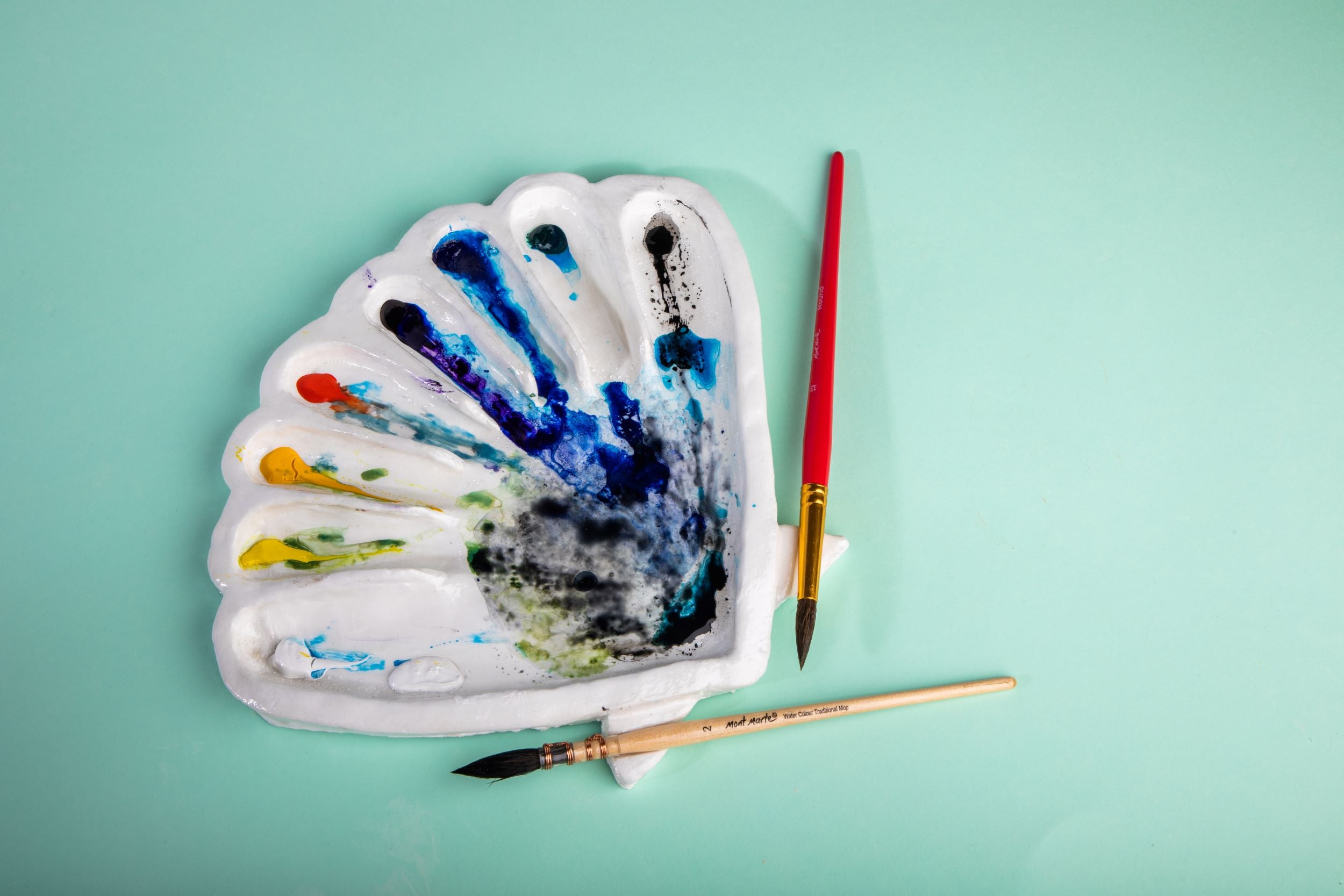 9. A seashell palette made from clay with watercolour paints and two brushes next to it