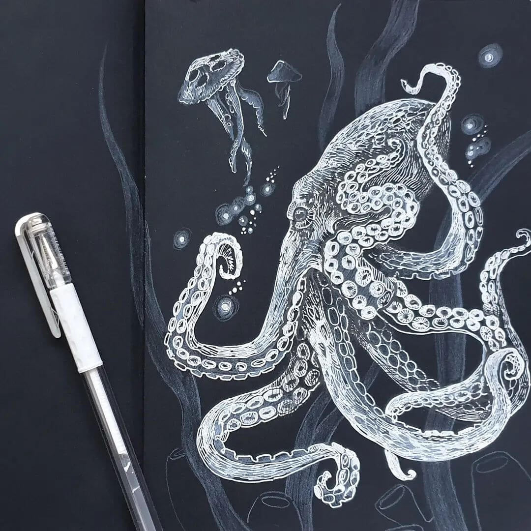 A white octopus drawn on black paper with a white pen next to the artwork.
