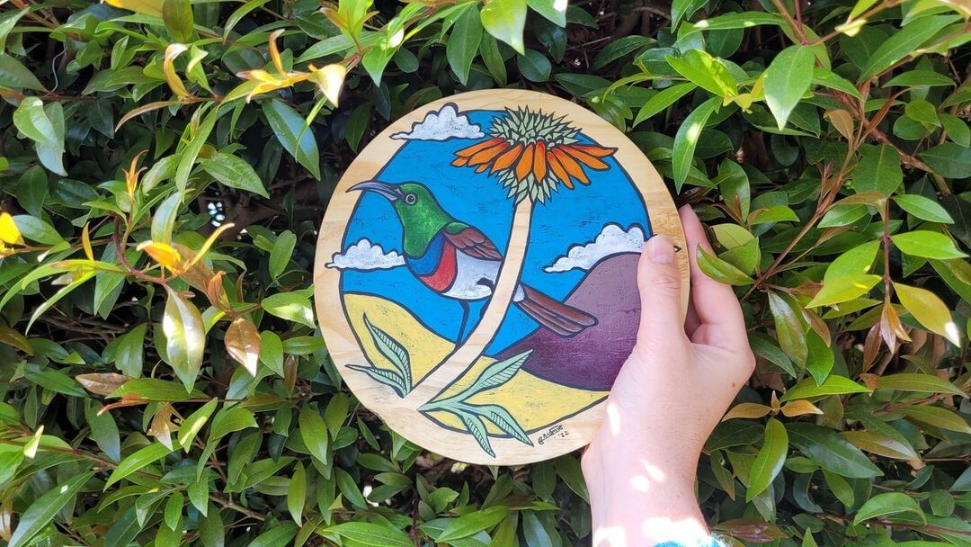 Hand holding a wooden circle of a painted bird.