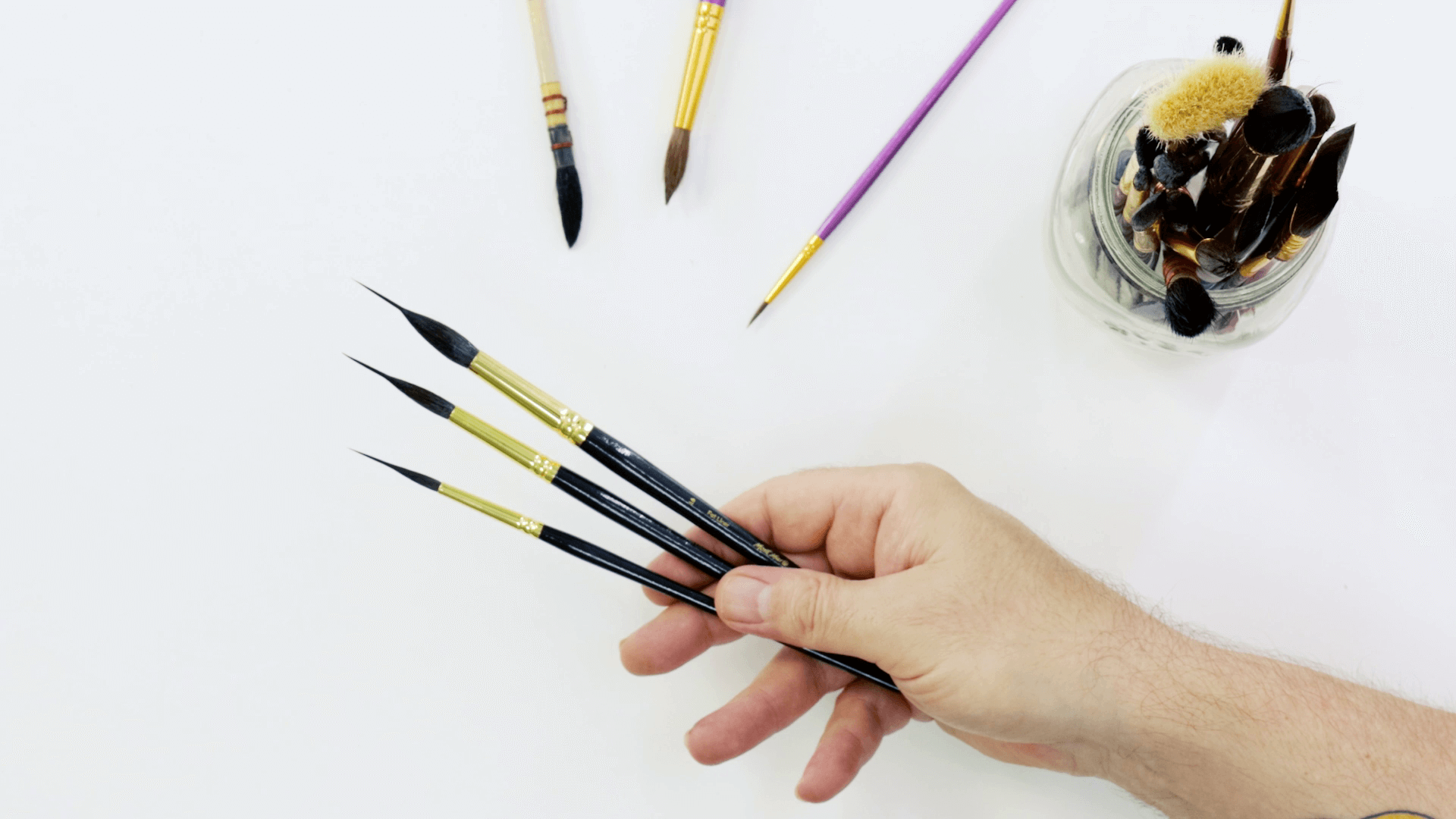 Hand holding three different sizes of fat liner watercolour brushes.