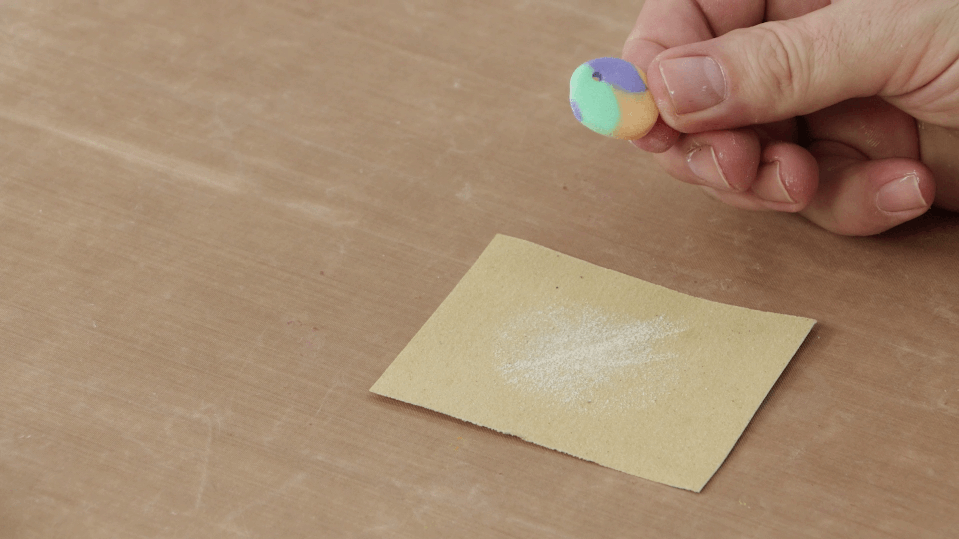 Hand holds a small circle of polymer clay next to sandpaper.