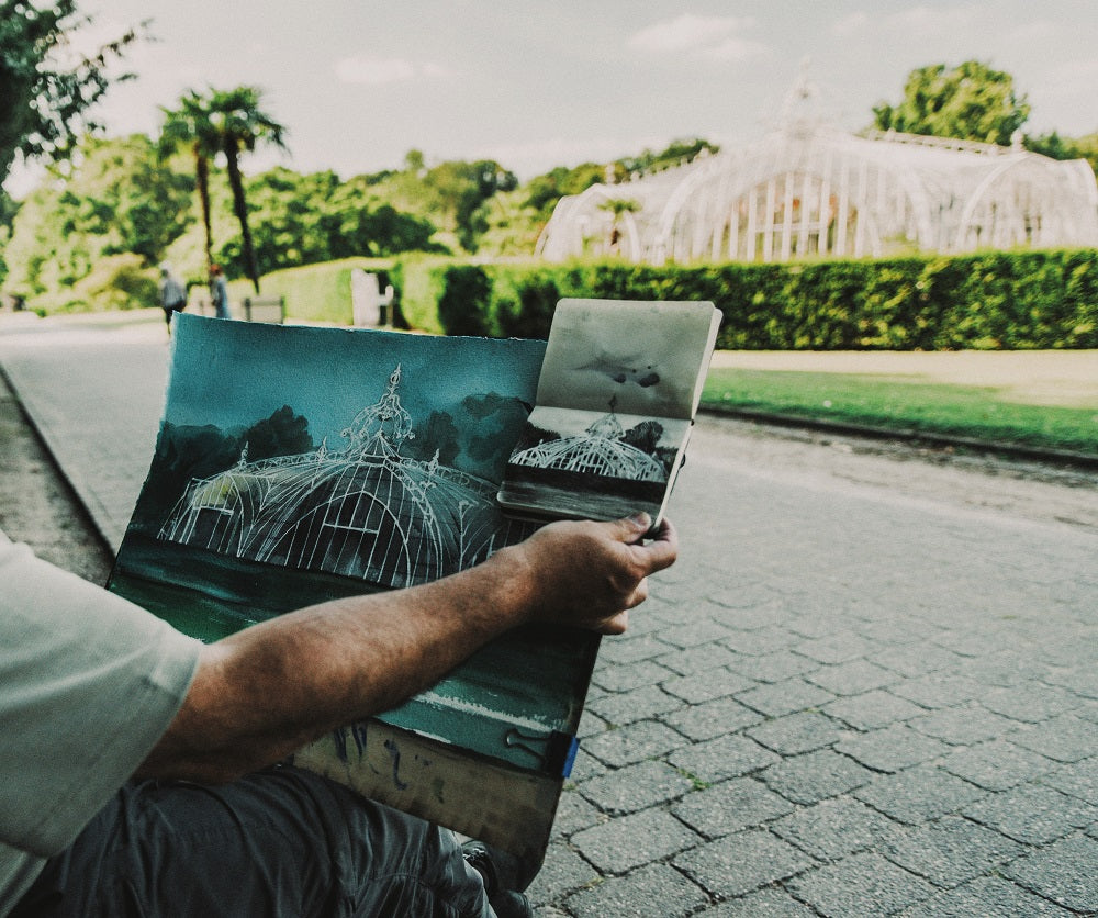 Man holds a board with a white greenhouse drawn in a garden.