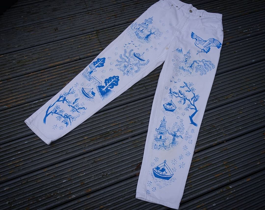 Pair of white jeans with an intricate blue hand painted design on them.