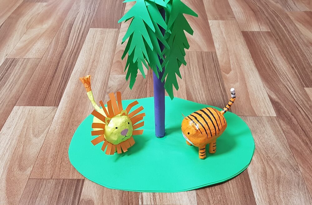Paper mache lion and tiger standing under a green paper tree.