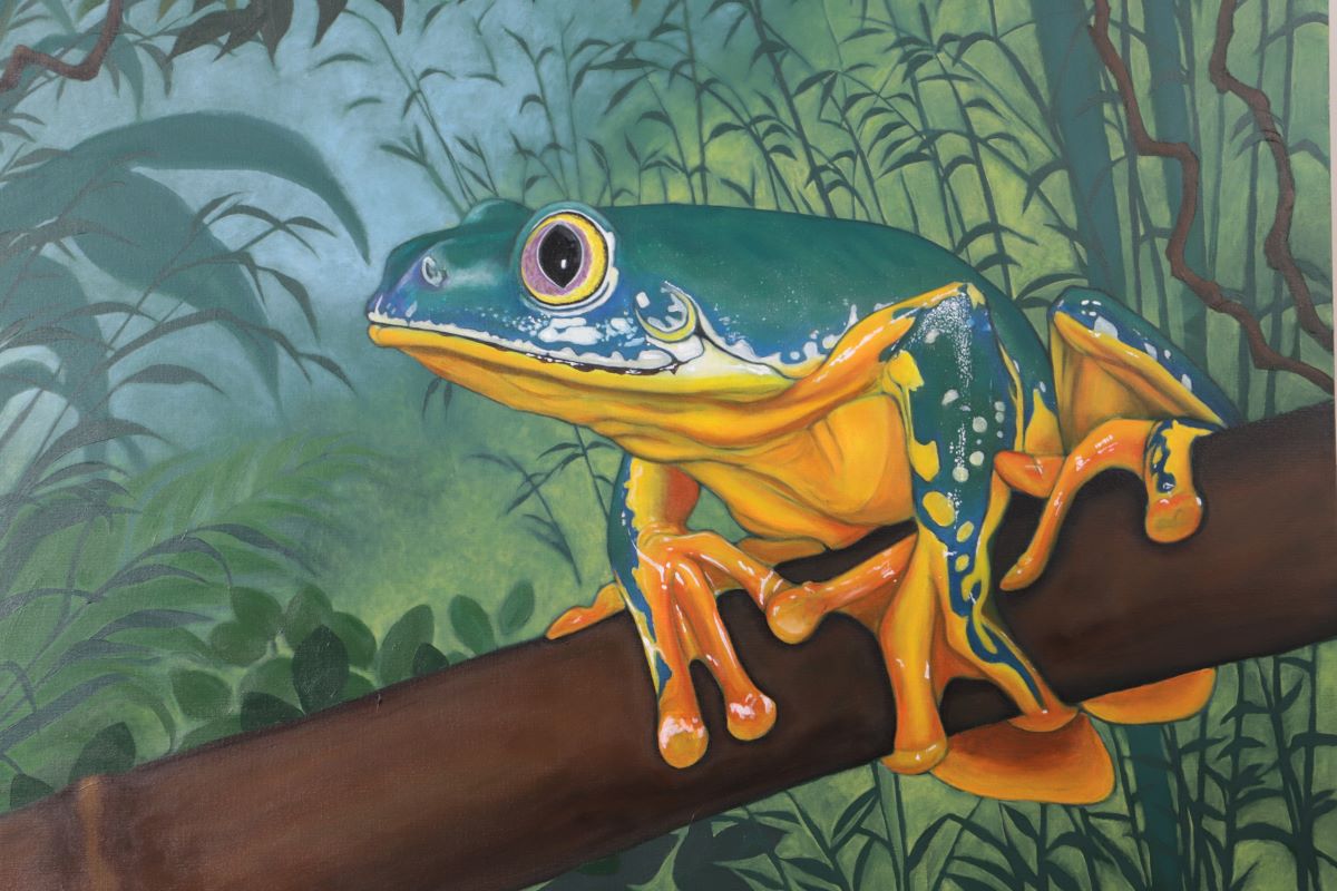 9. @montmarteart artwork of a green frog sitting on a branch with yellow feet, belly, and eyes