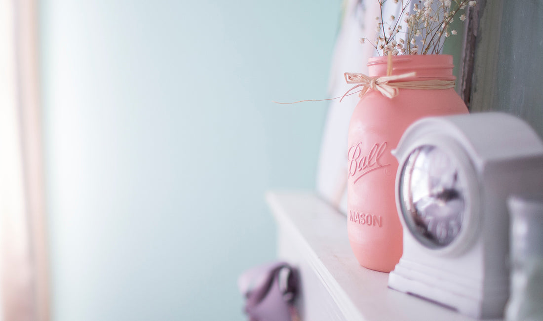 A pink painted mason jar on a mantlepiece.