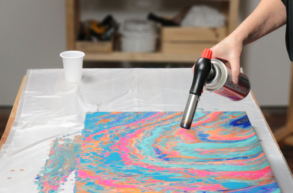 Blow torch being used on painting done with pouring paint.
