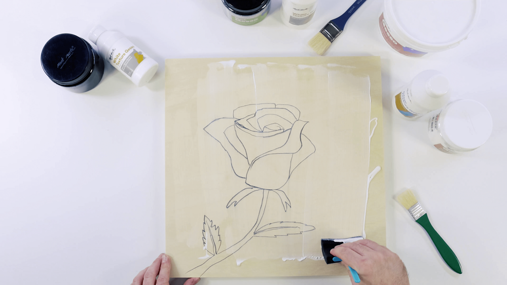 A hand painting gesso with a foam sponge brush over the top of a rose drawing drawn in graphite.