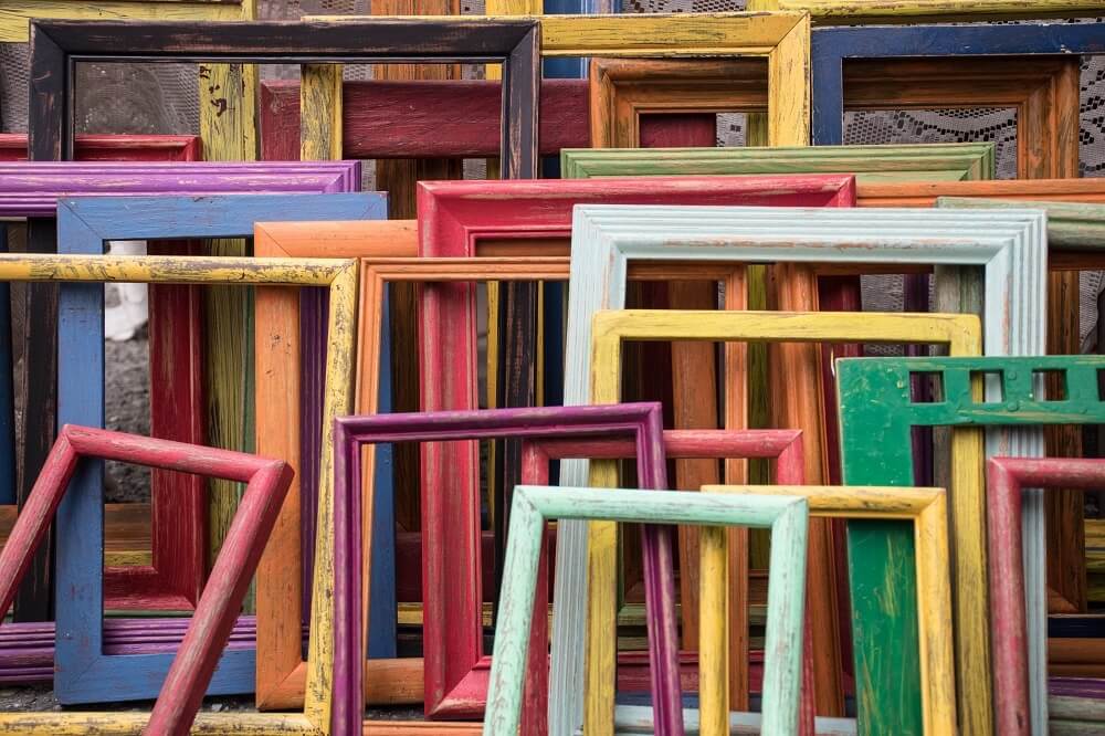 Empty coloured frames resting on ground of various colours and sizes. 
