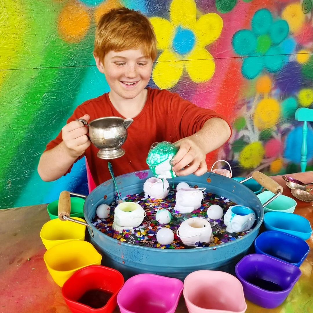 A child doing sensory play with lots of rainbow cups, liquid, and glitter