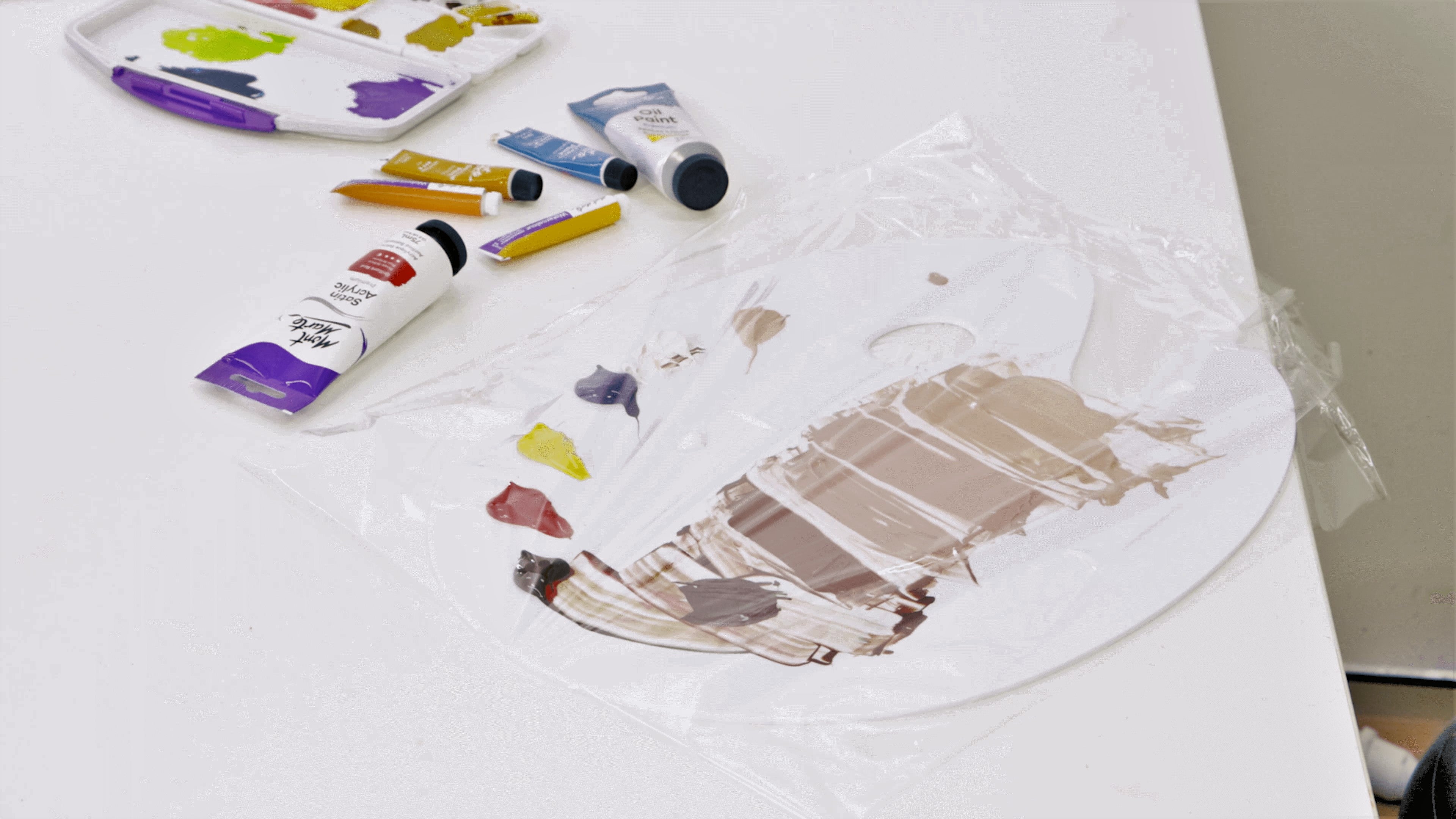 A used paint palette with acrylic paint on it, covered in cling wrap to store the palette