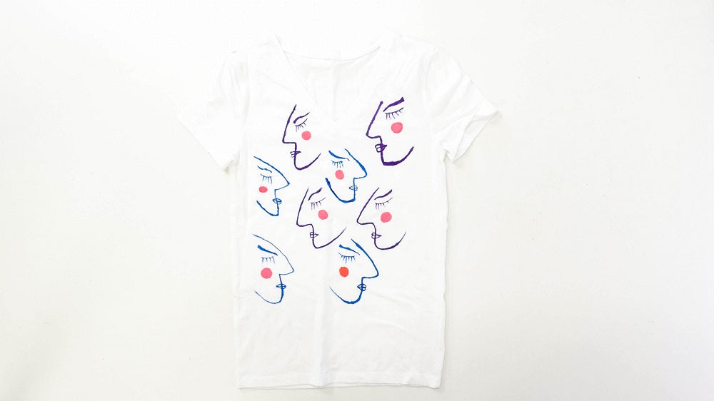 A white t-shirt with purple and blue Matisse style faces drawn on using Mont Marte Dual Tip Fabric Markers 24pc.