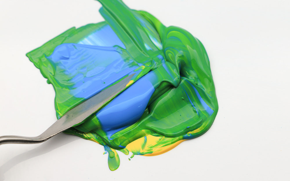 Blue, green, and yellow paint being mixed with a palette knife