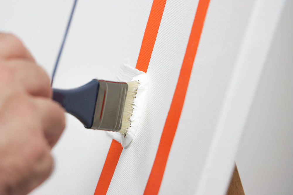 White paint being brushed thickly onto a canvas with orange stripes