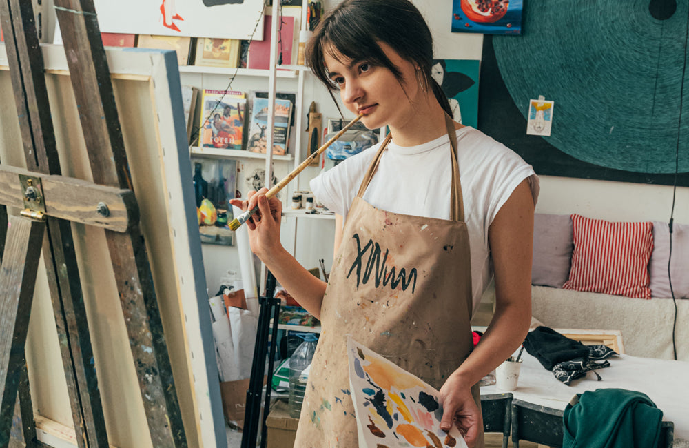 Painter wearing an apron looking at their work while standing in a studio