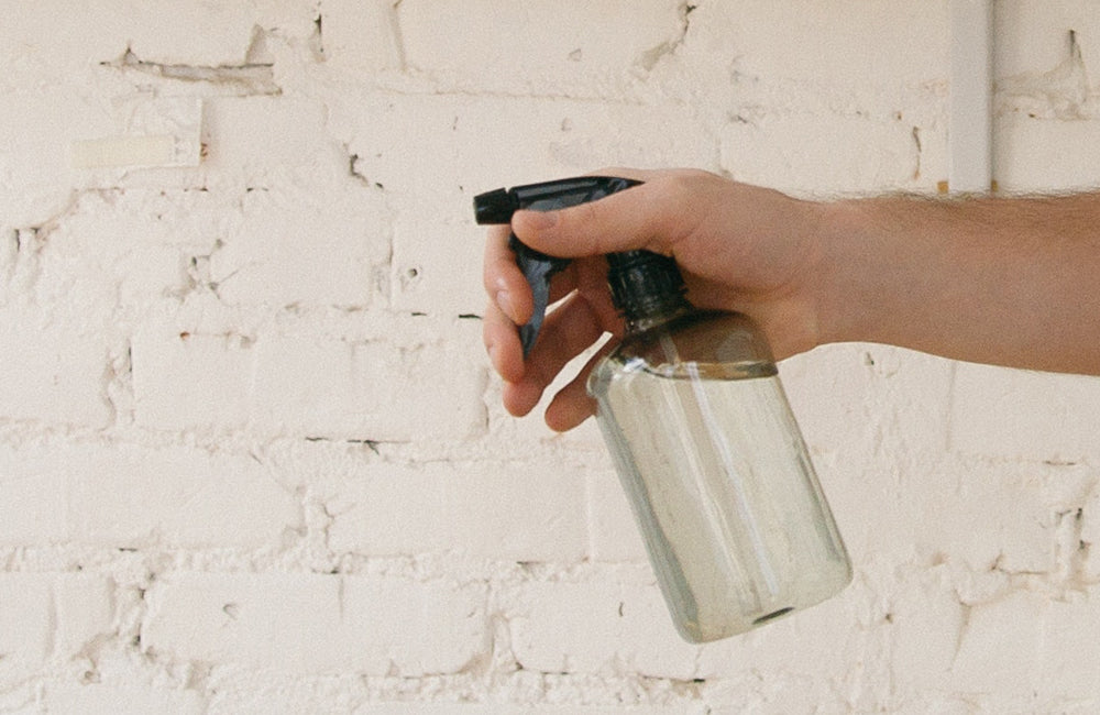 Spray bottle being held in front of a white brick wall