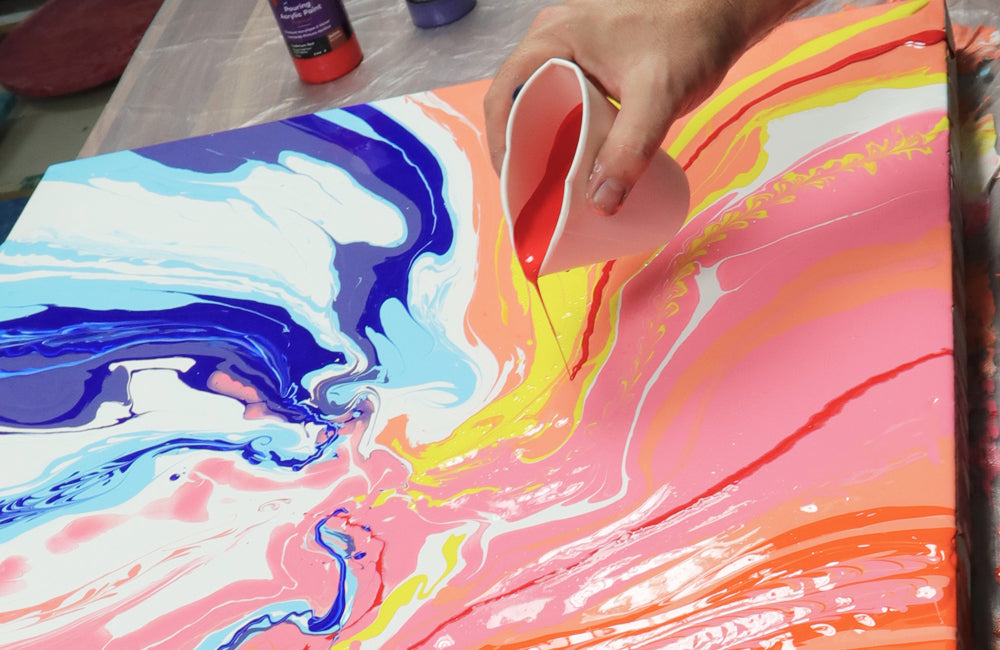 A pouring paint cup filled with red paint being squished inwards to create a thinner pouring spout