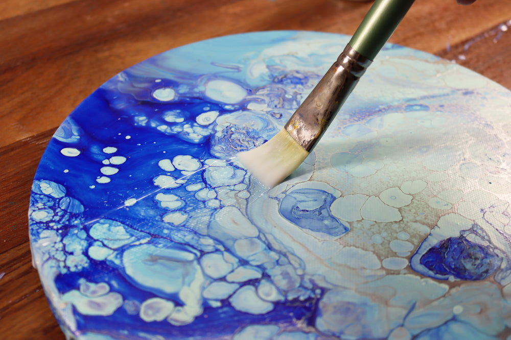 Acrylic medium gloss being painted onto a finished pouring project on a circular painting surface