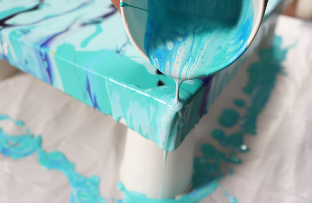 Pouring paint in shades of blue being poured over the corner of a canvas 