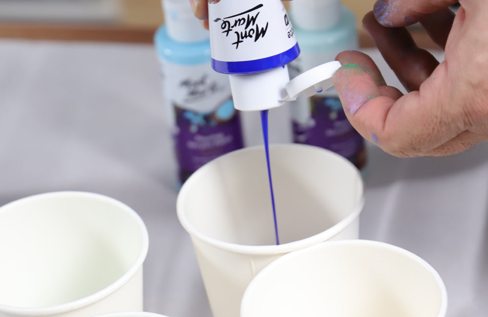 Blue paint being poured from a paint bottle into a white cup