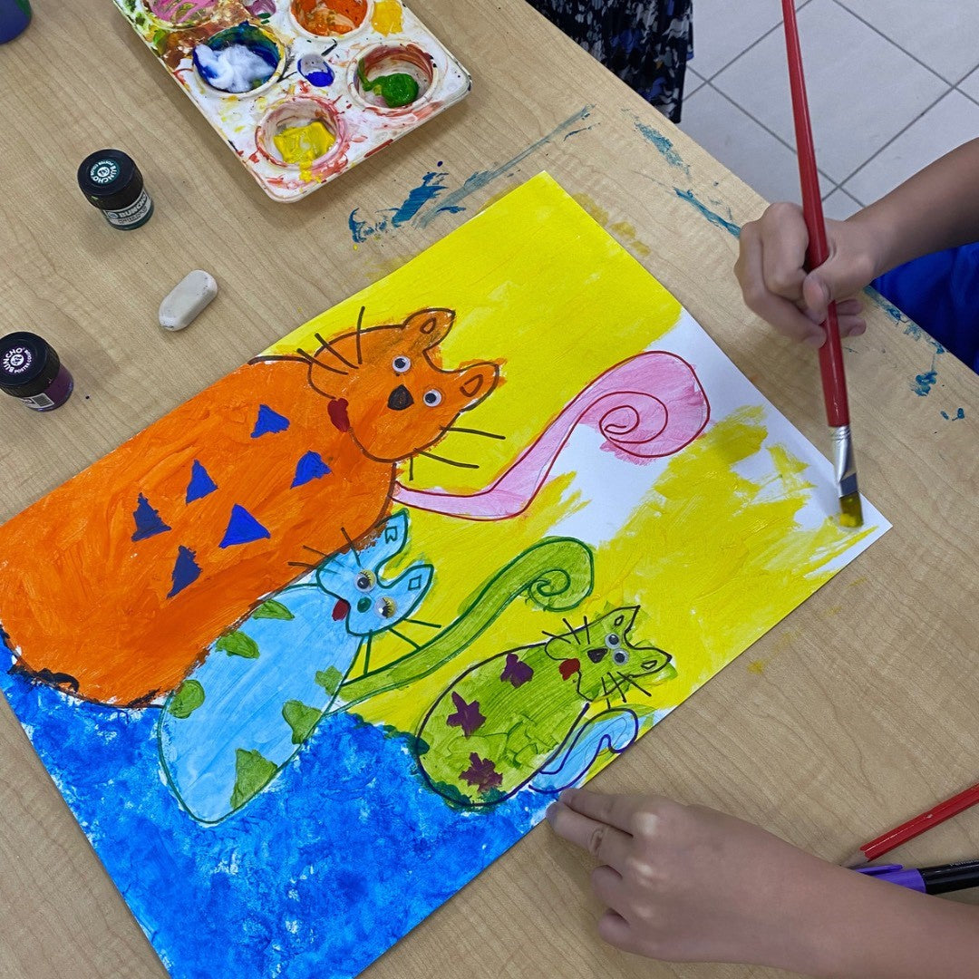 Child painting a picture of three different coloured cats