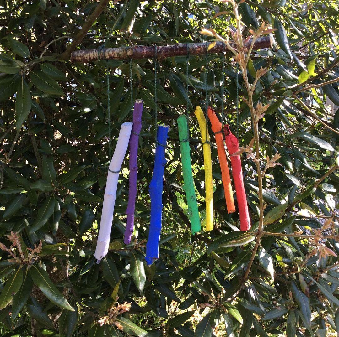 Brightly coloured, rainbow sticks made into a mobile hanging from a tree.