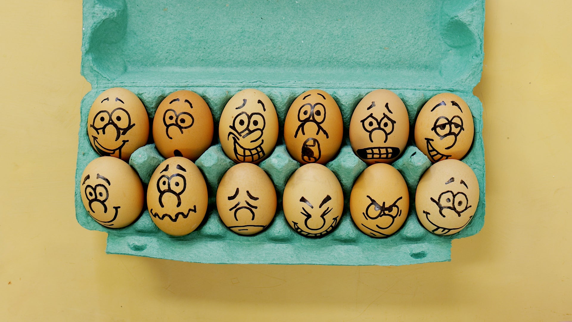 A green egg carton with funny faces drawn on each egg.