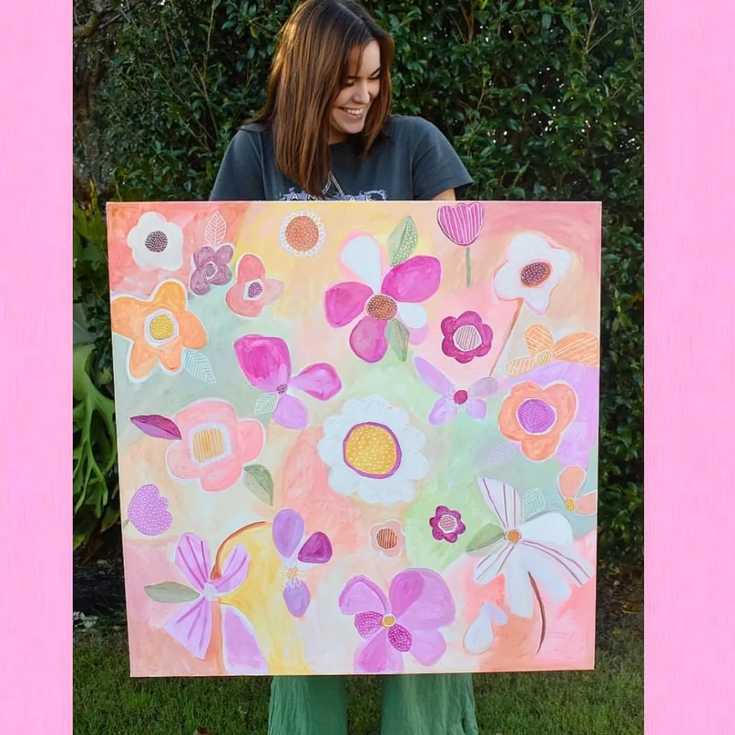 Emily holding one of her bright floral paintings against a green leafy background