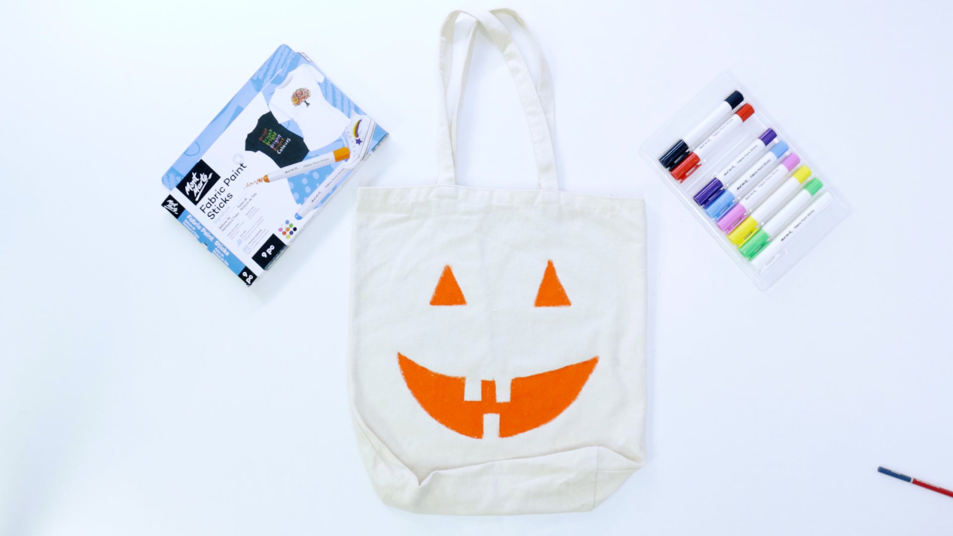 A tote bag with a pumpkin face sitting next to fabric markers.