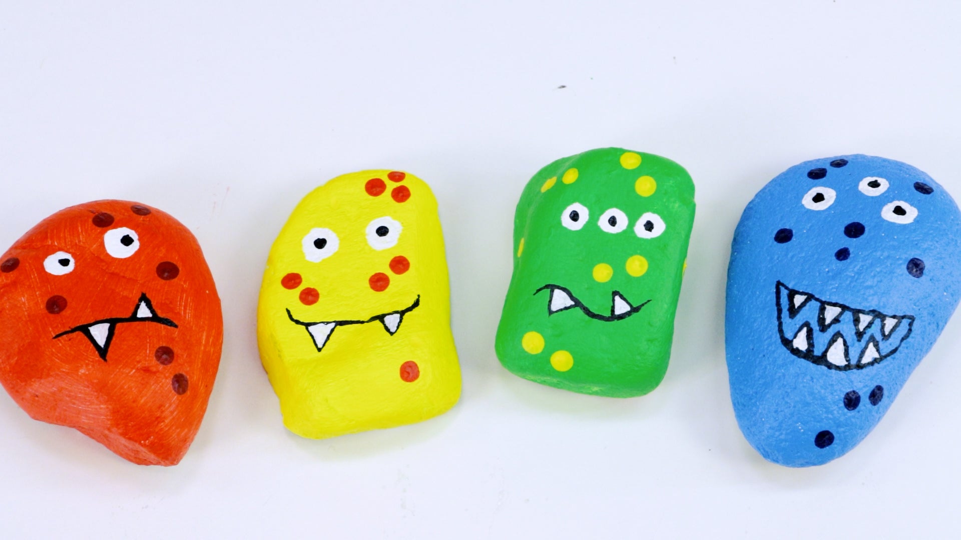 Four rocks painted to look like colourful monsters sitting side by side.