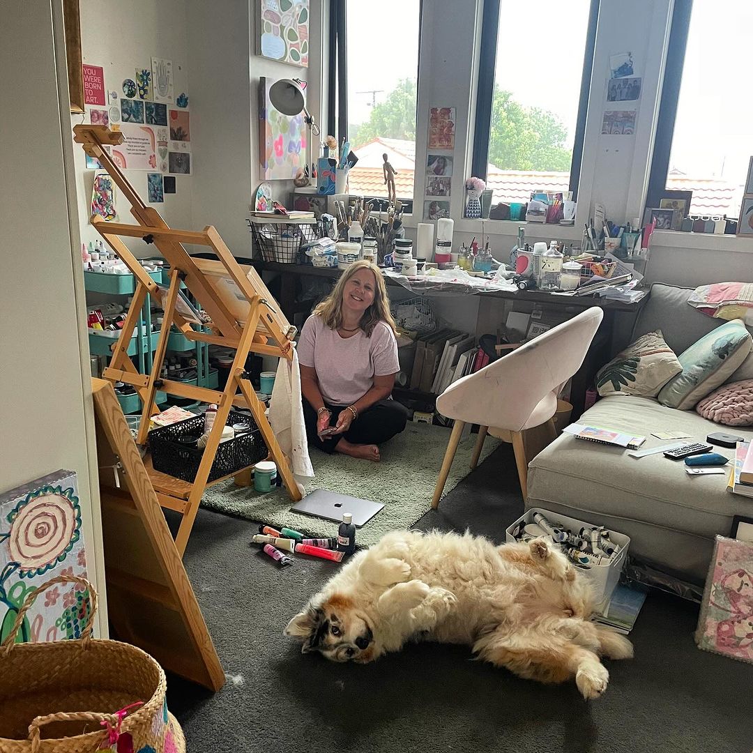 Kerrie sitting in her studio with her dog surrounded by creative supplies