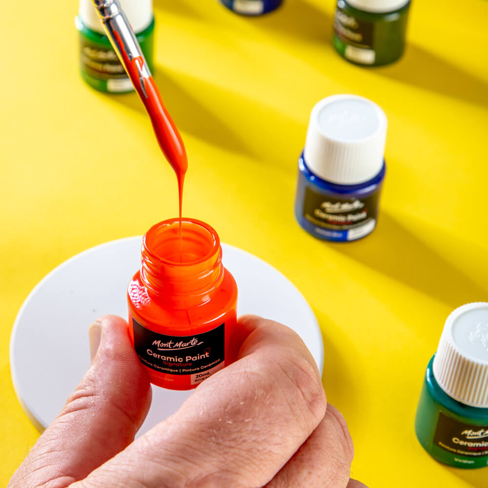 Mont Marte red ceramic paint being dripped from a brush into the jar