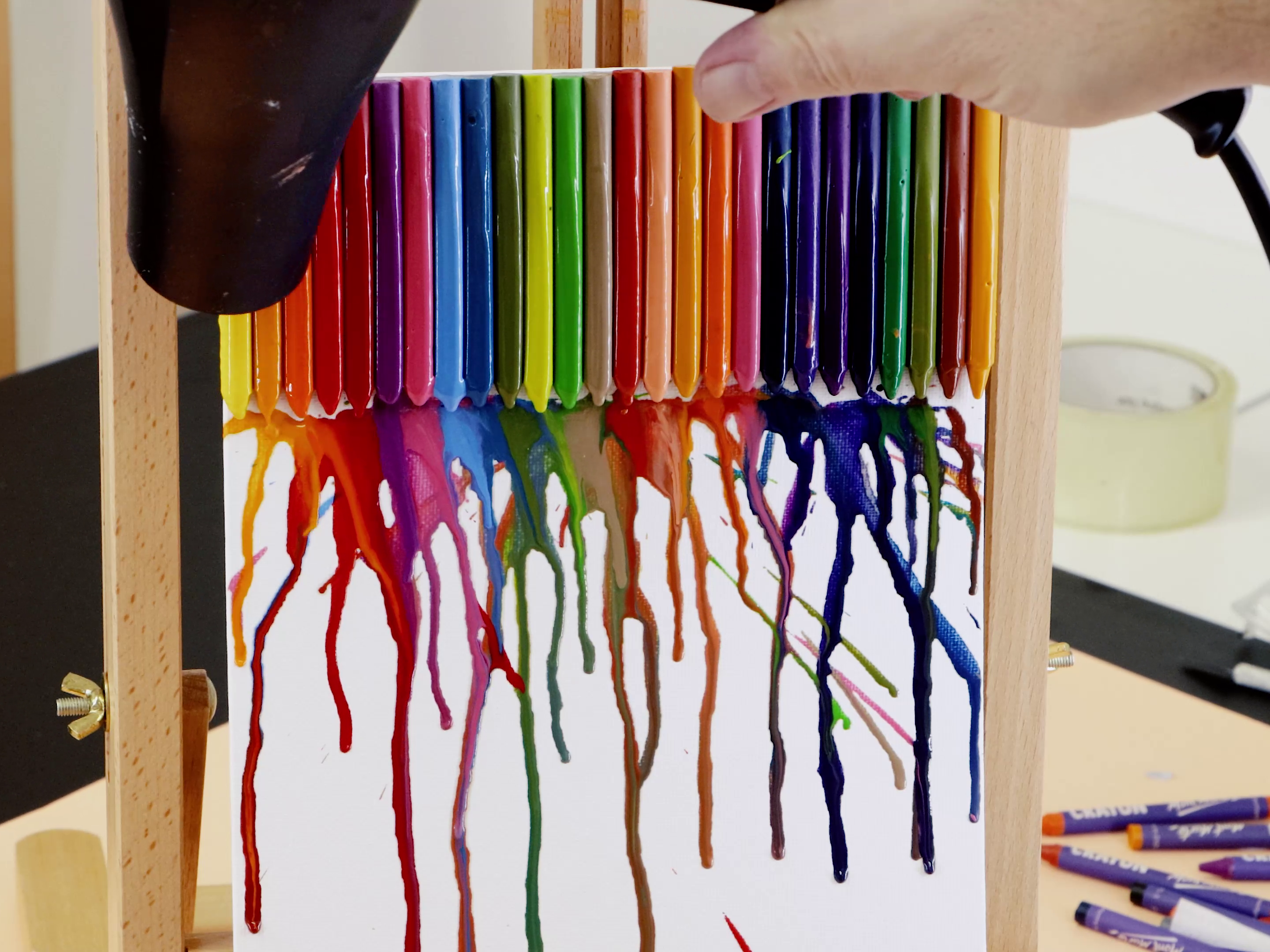 Rainbow crayons stuck to a canvas being melted with hair dryer