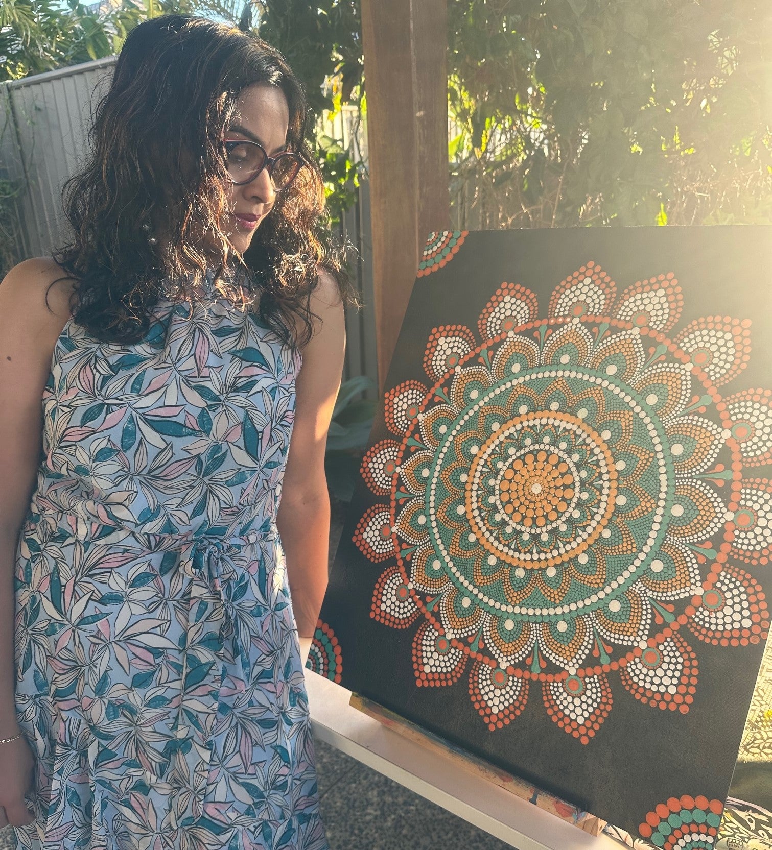 Suchi looking down at one of her mandala artworks, bathed in sunlight