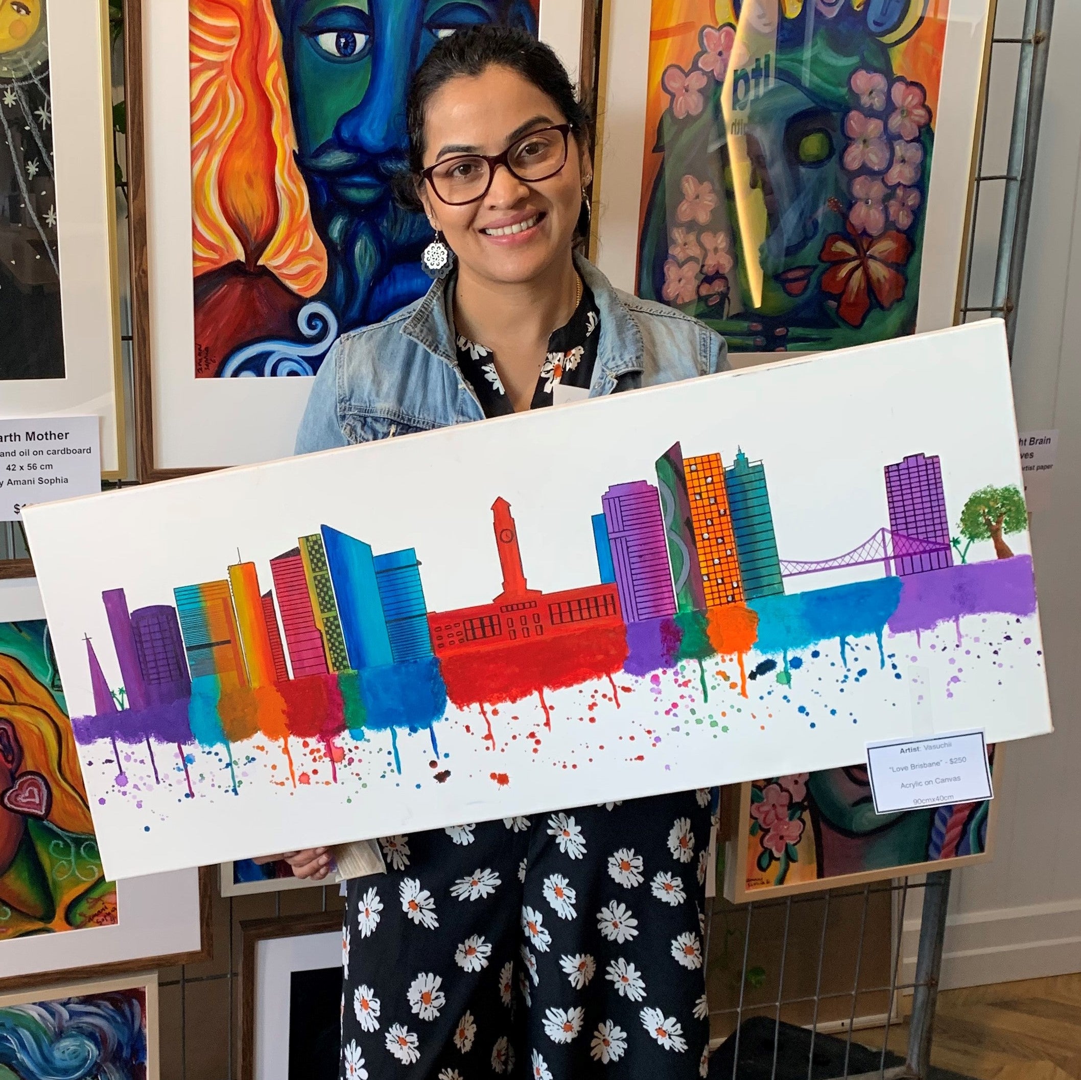 Suchi standing in an art exhibition holding her cityscape painting