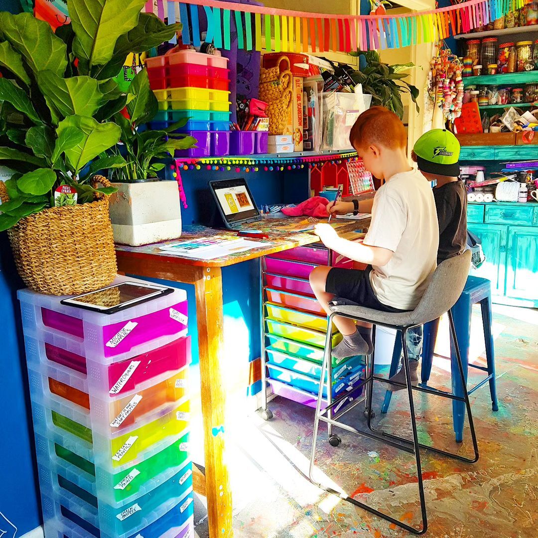 Two children sitting at a rainbow desk in a colourful room