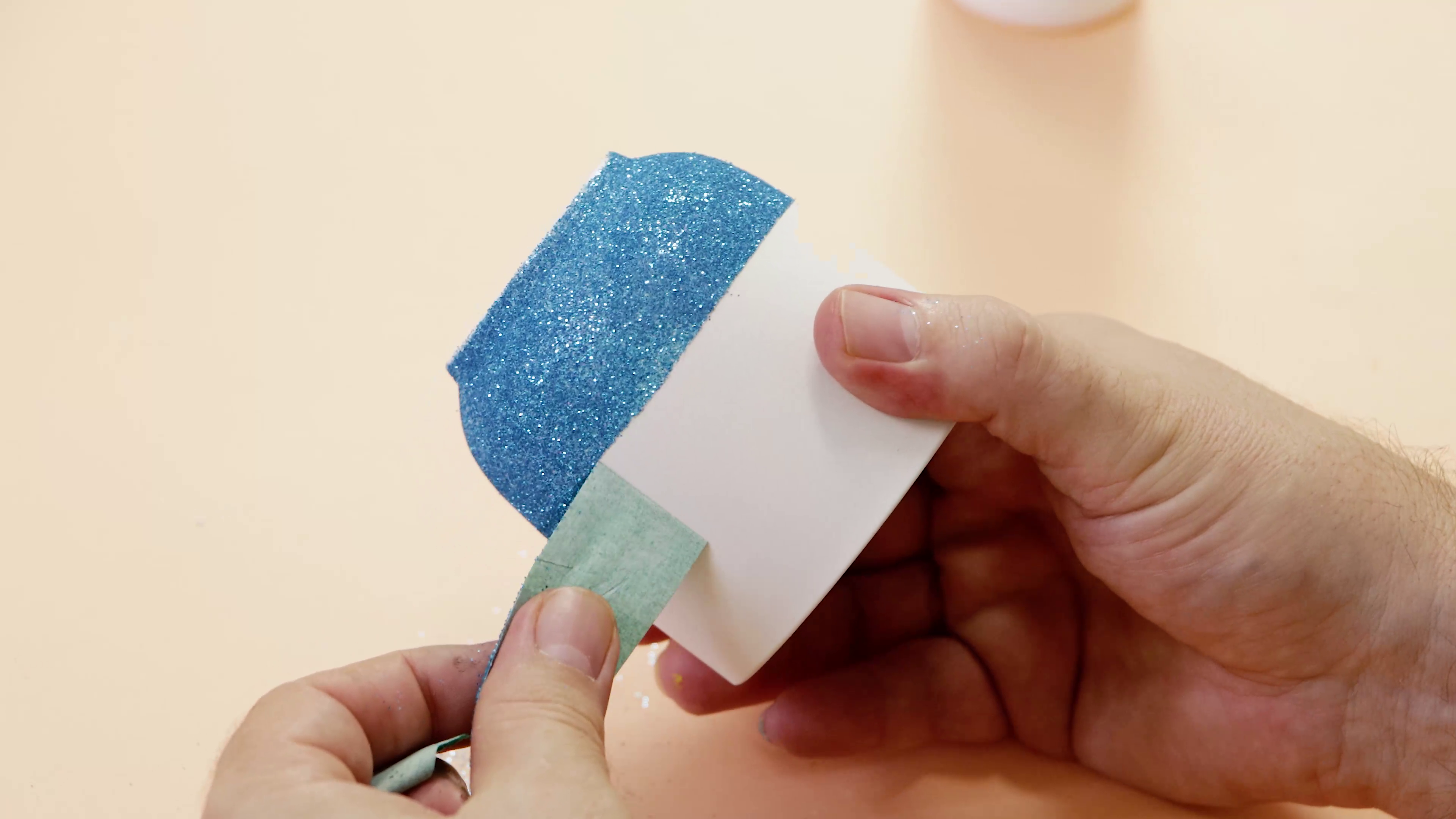 Cup being decorated with blue glitter on the bottom half