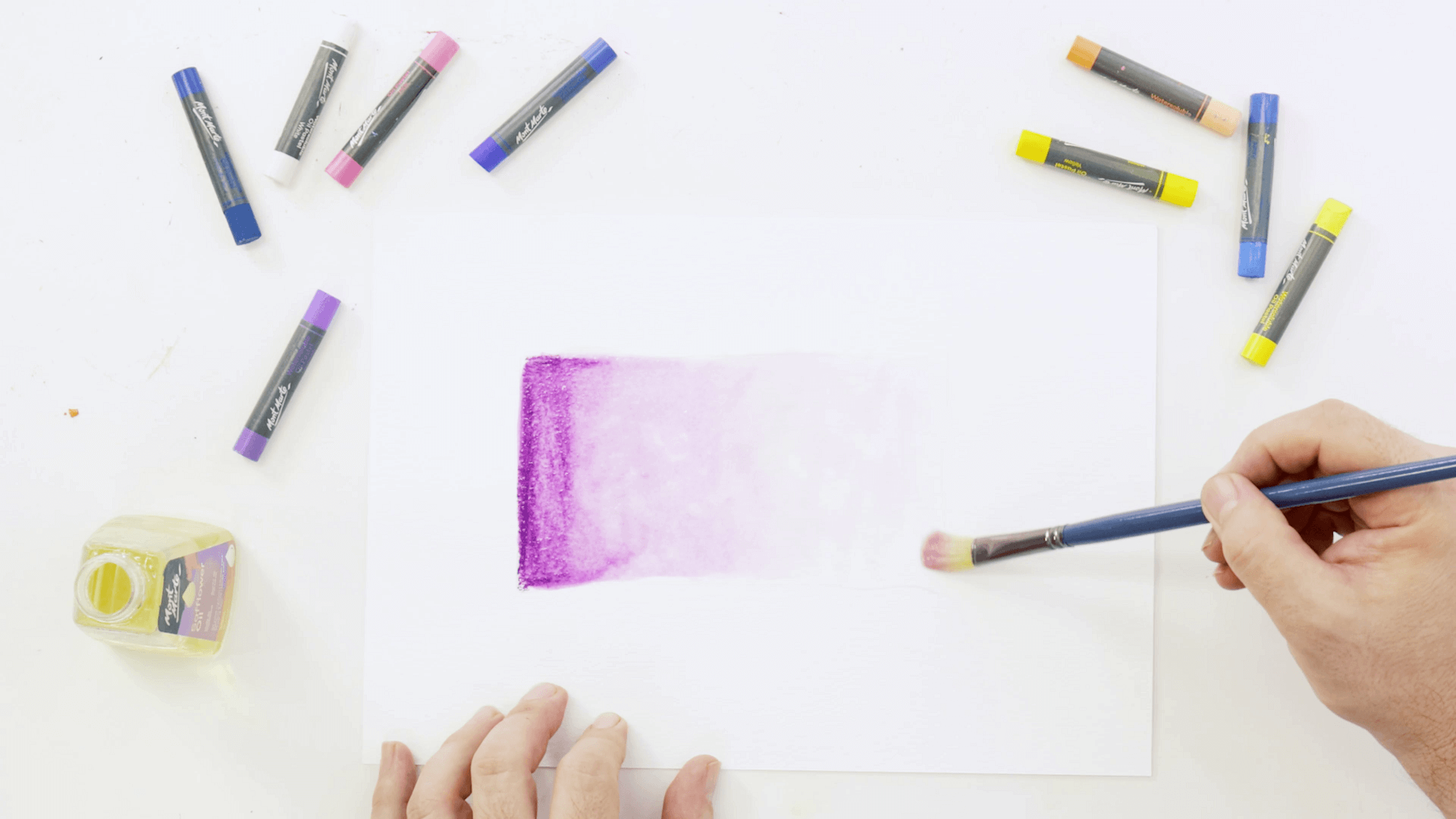 Hand activating watersoluble oil pastels with a paint brush for a watercolour effect.