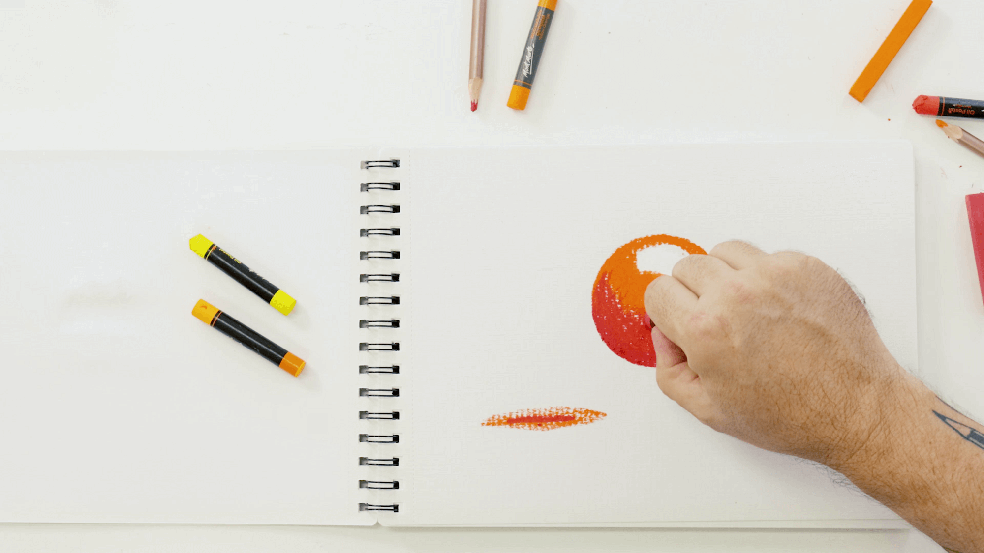 Hand colouring an orange circle with oil pastels to blend.