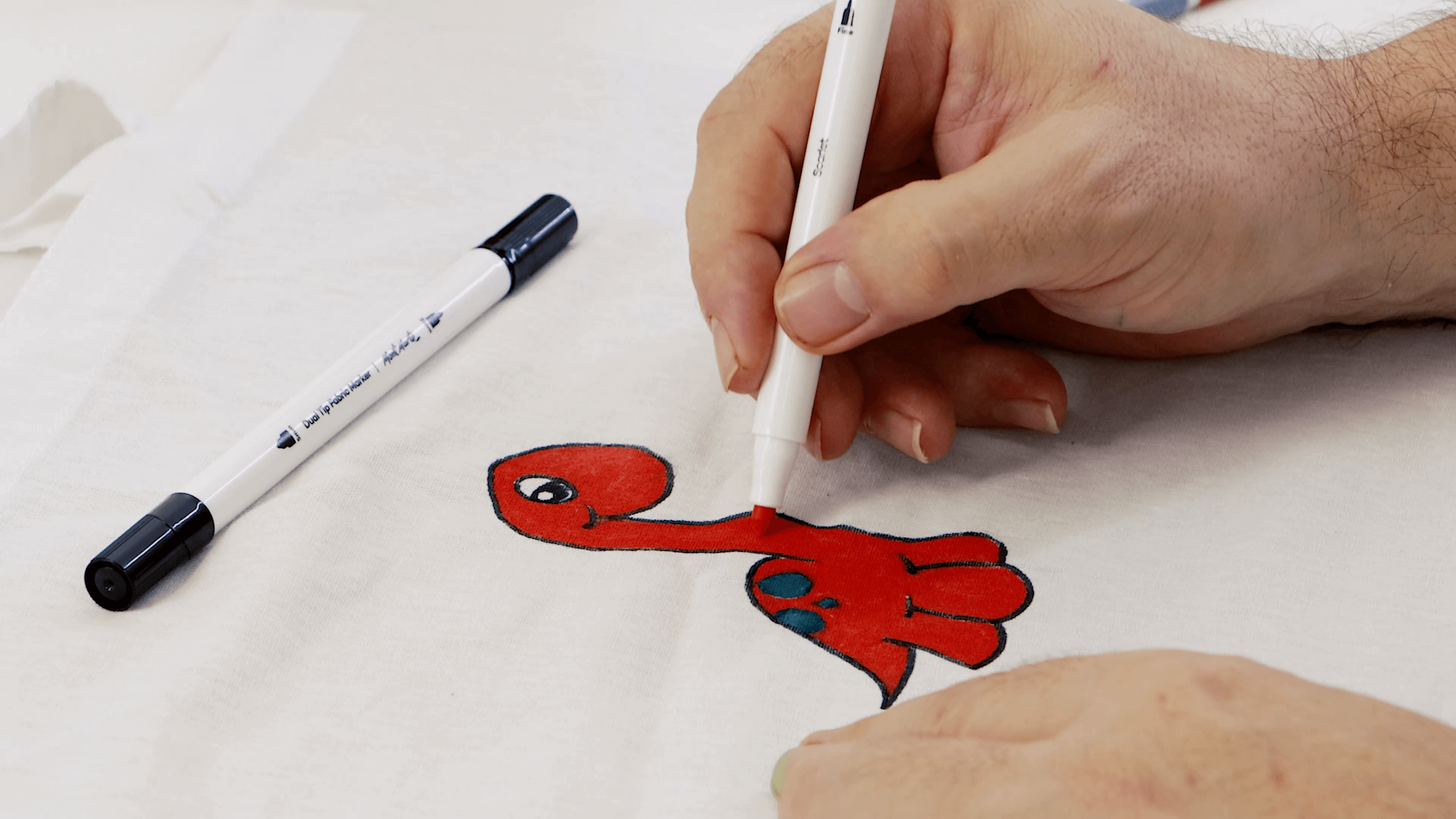 Hand drawing a dinosaur on white fabric using a fabric marker.