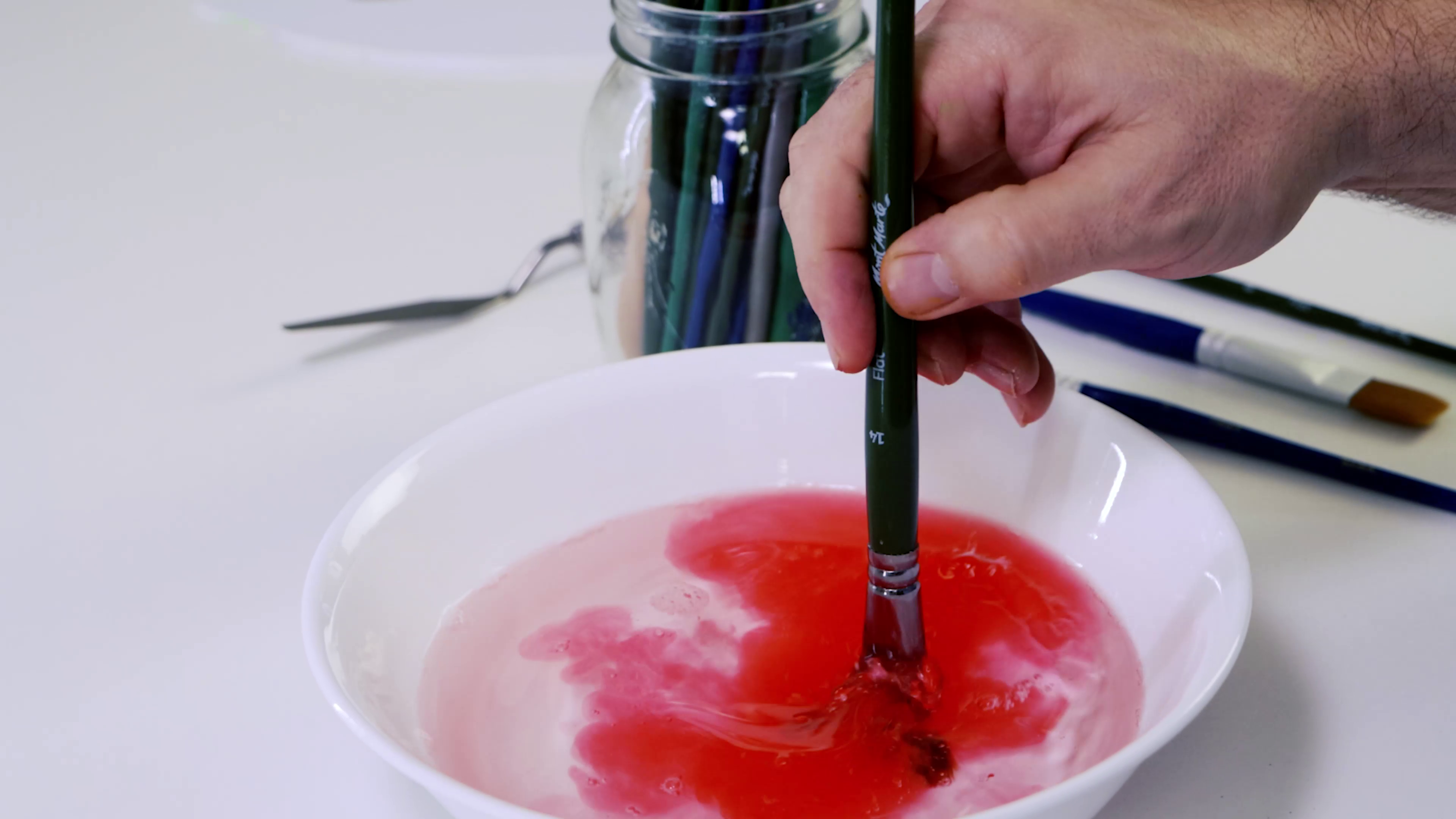Red paint being washed off an acrylic paint brush