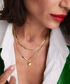 Woman wearing a Beaded Pendant Necklace, featuring a handcrafted 14k gold bar and chain. The close-up highlights the necklace's elegant design and the woman's lips.